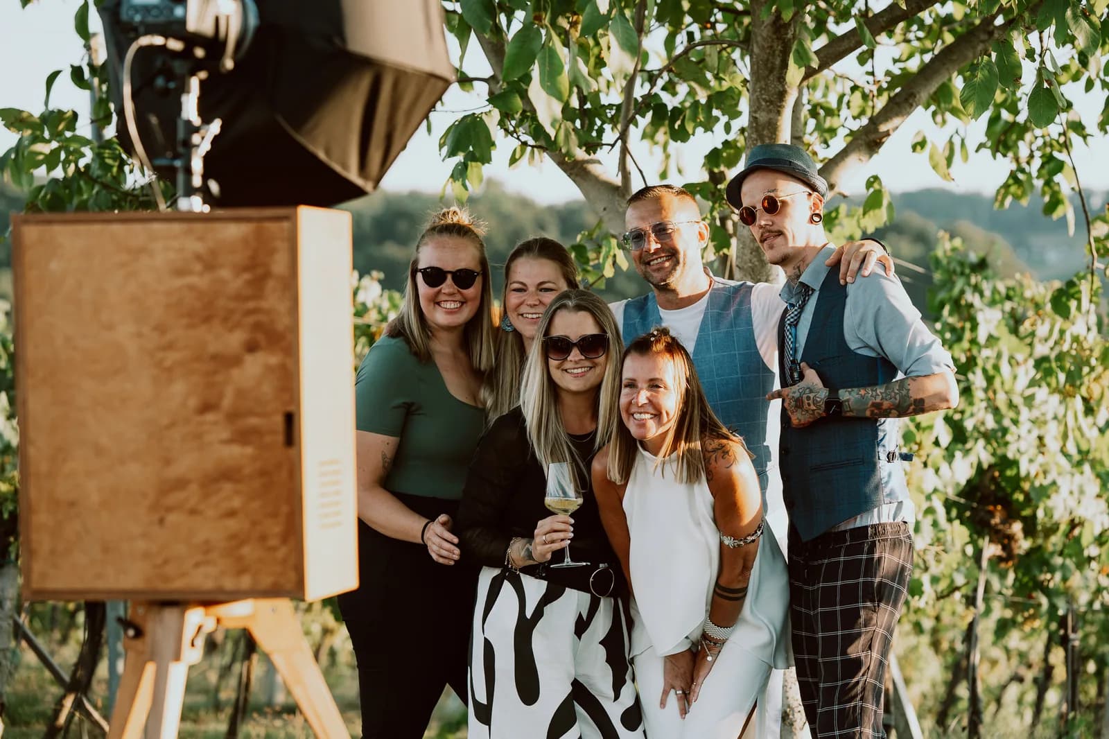 Fröhliche Gruppe posiert vor der Vintage Fotobox im Weinberg