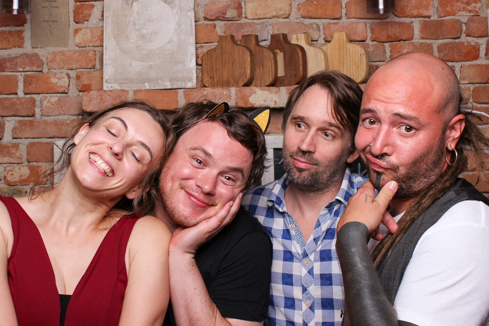 Eine Gruppe von vier Personen lächelt, während sie kreativ mit Fotobox-Accessoires posiert.