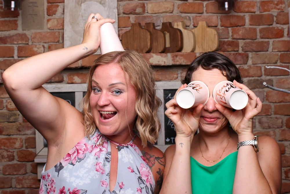Zwei Frauen in der Fotobox mit Pappbechern auf dem Kopf, die für einen lustigen Moment sorgen.