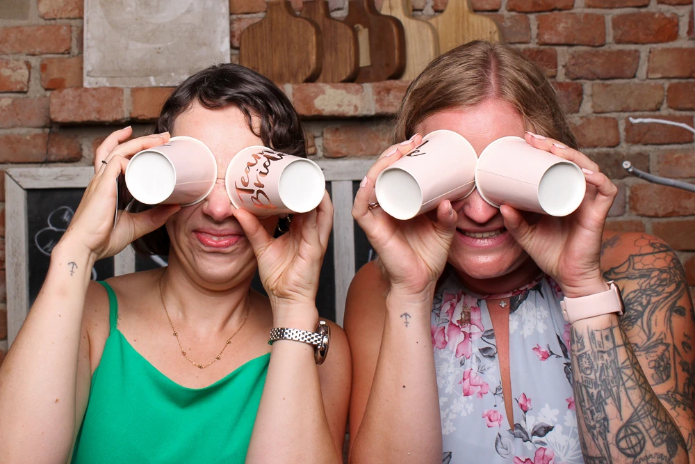 Zwei Frauen posieren in der Fotobox mit Pappbechern als Ferngläser vor den Augen.