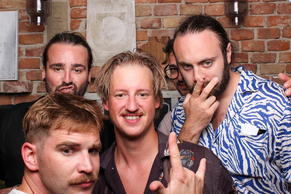 Fünf Männer posieren fröhlich und machen witzige Gesten in der Fotobox bei einer Party.