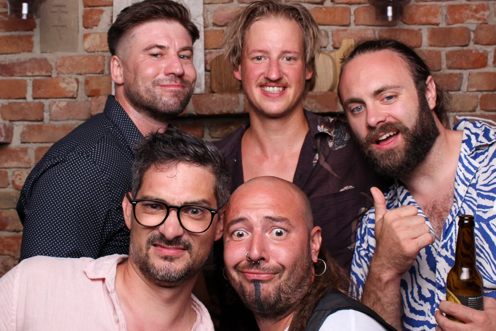 Fünf Freunde stehen in der Fotobox, lächelnd und in Feierlaune, bereit für lustige Fotos.